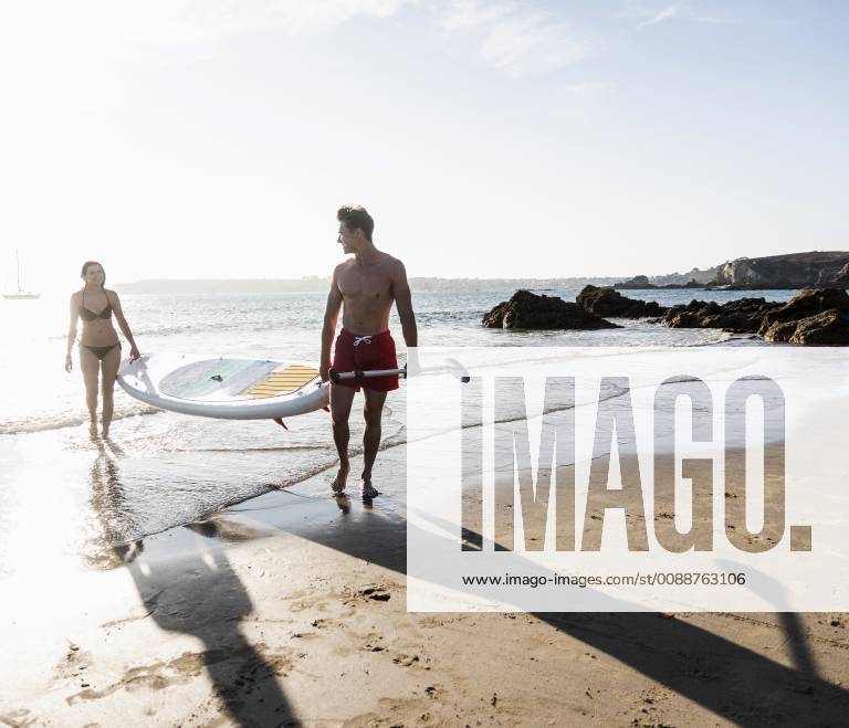 France, Brittany, young couple carrying an SUP board at the sea together model released Symbolfoto UUF15925
