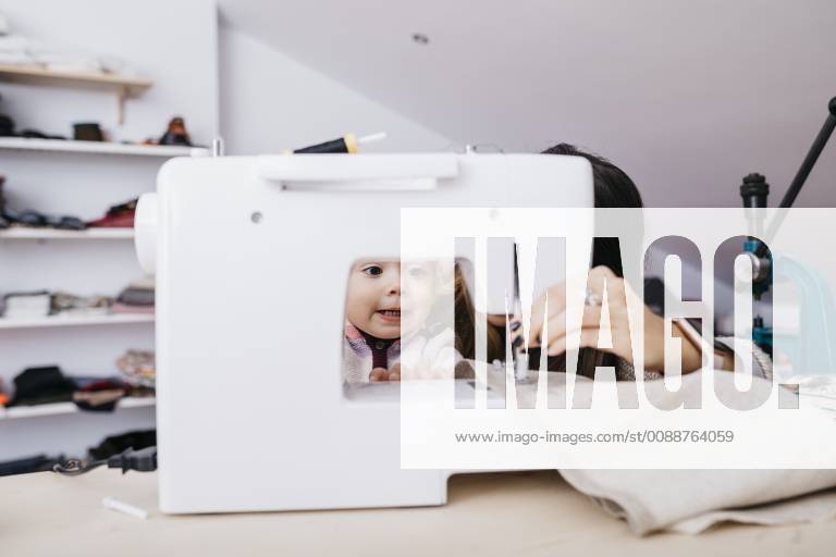 Little daughter watching her mother using sewing machine at home model released Symbolfoto property released JRFF02085