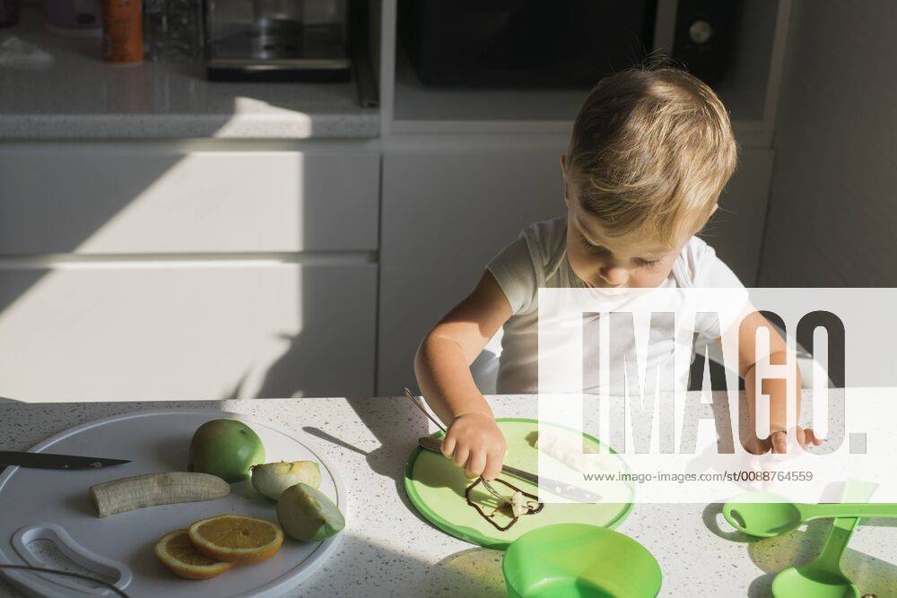 Little boy sitting at table in the kitchen eating fruits model released Symbolfoto property released MOMF00533