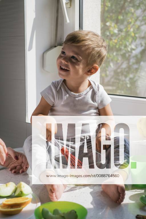 Portrait of smiling little boy sitting barefoot on worktop in the kitchen whisking eggs model released Symbolfoto property released MOMF00534