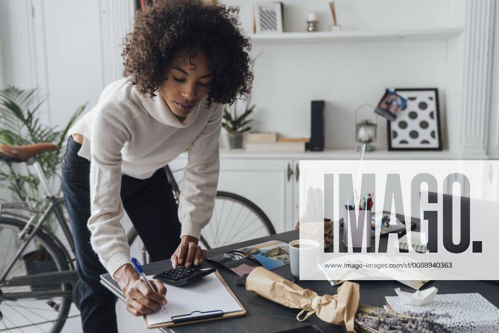 Freelancer standing at hert desk, using calculater, taking notes model released Symbolfoto property released BOYF00930