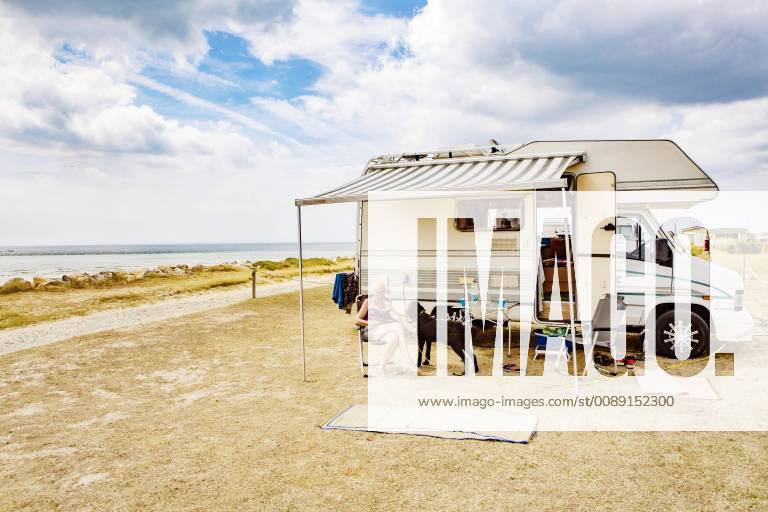 Woman sitting on holiday with a dog king poodle in front of her camper by the sea Portbail Normandy France Europe