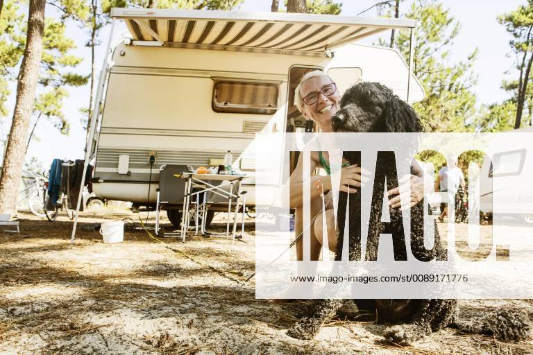 Woman crouches laughing with her dog king poodle in front of camper on a camping site le Gurp Grayan et l Hopital Aquitanien Gironde France Europe