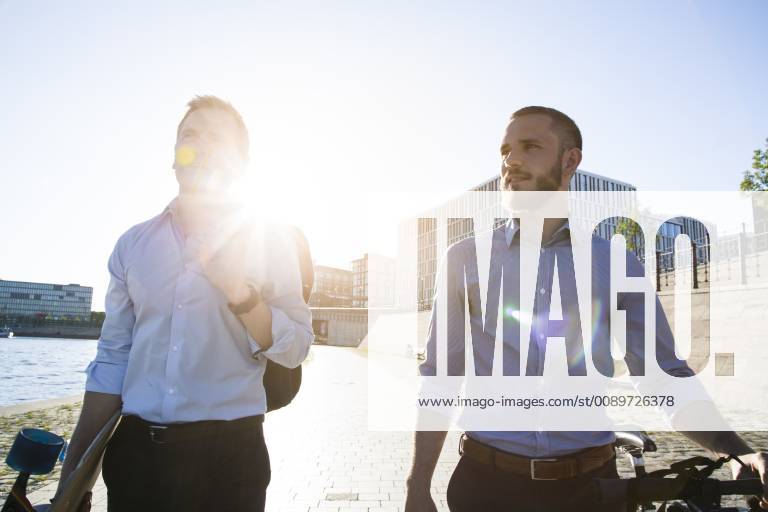 Two businessmen walking with bicycle and skateboard at the riverbank model released Symbolfoto FKF02591