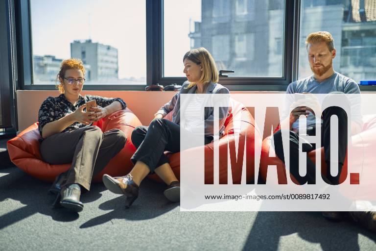IMAGO Creative: Business - Work-Life Balance Colleagues with cell phones sitting in bean bags in office lounge model released Symbolfoto property released ZEDF00987