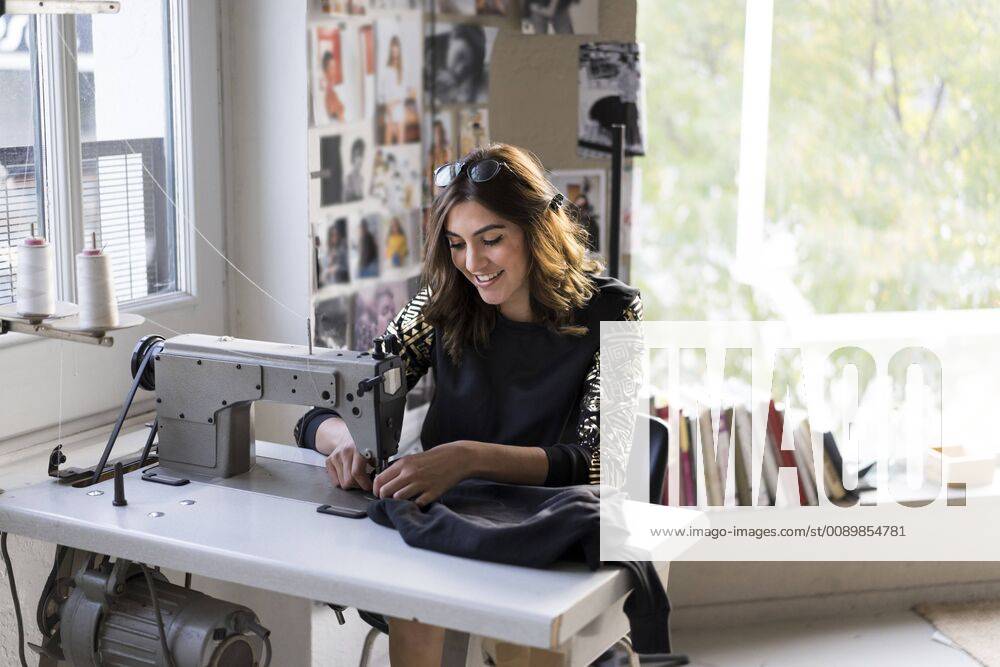 Smiling young fashion designer using sewing machine in her atelier model released Symbolfoto property released AFVF02054