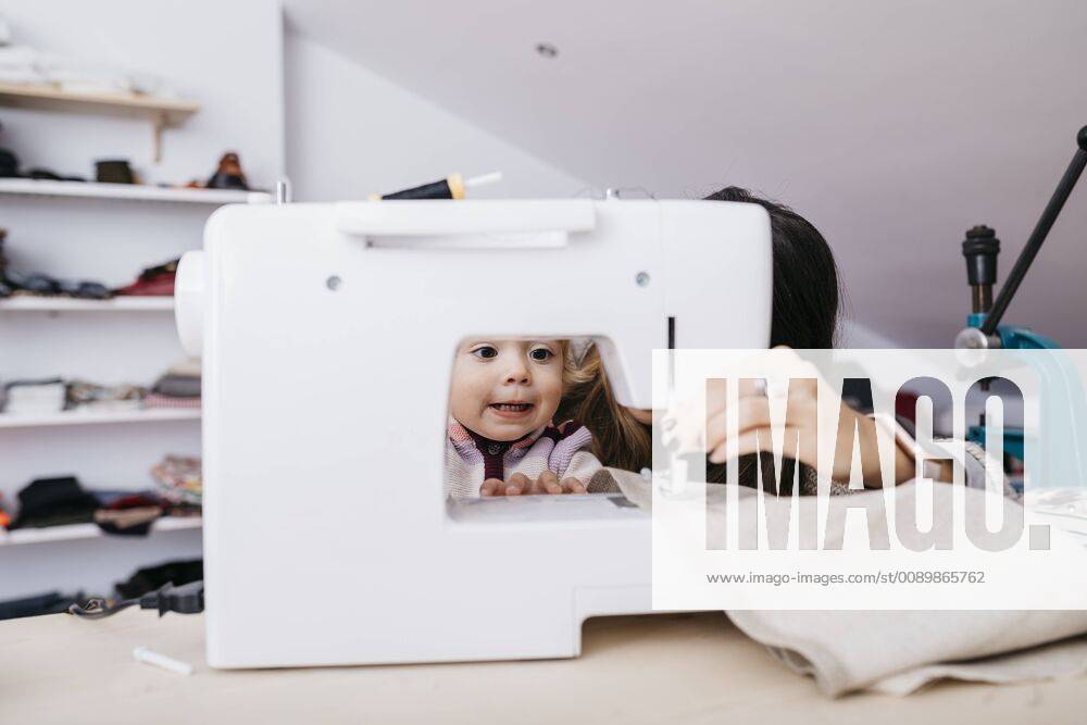 Little daughter watching her mother using sewing machine at home model released Symbolfoto property released JRFF02085