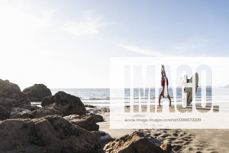 France, Brittany, young man doing a handstand and woman holding surfboard on the beach model released Symbolfoto UUF15913