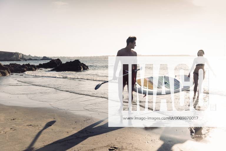 France, Brittany, young couple carrying an SUP board at the sea together model released Symbolfoto UUF15924