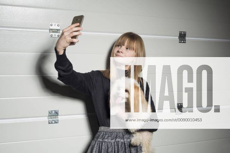 Girl with dog taking selfie with camera phone in garage
