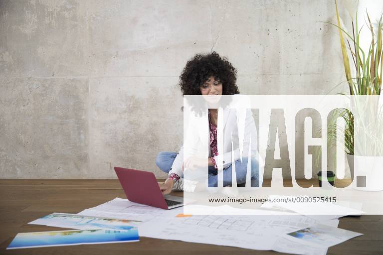 Businesswoman sitting on the floor in a loft working with laptop and documents model released Symbolfoto property released FKF03195