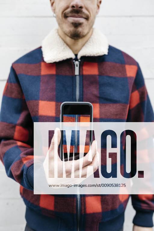 Young man showing a photo on the phone in the colors of his jacket model released Symbolfoto property released JRFF02564