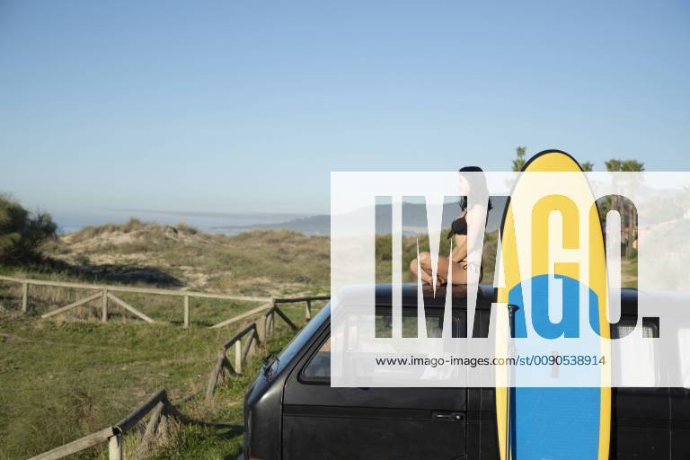 Spain, Andalusia, Tarifa, woman sitting on roof of a camper van stand up paddle board at the coast model released Symbolfoto KBF00389