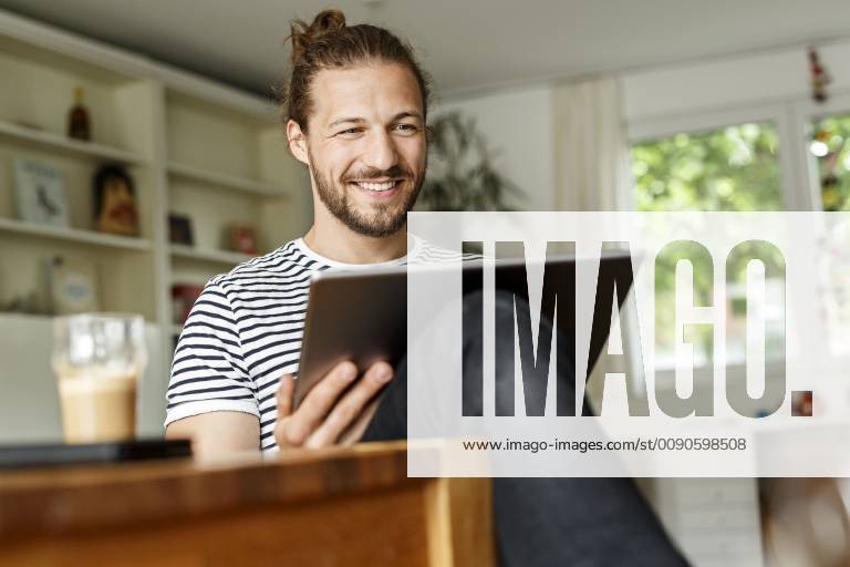 Young man with a bun sitting at home, using digital tablet model released Symbolfoto property released PESF01140