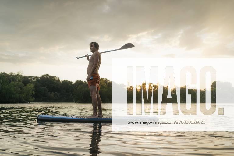 Man standing on SUP board on a lake at sunset model released Symbolfoto GUSF01826