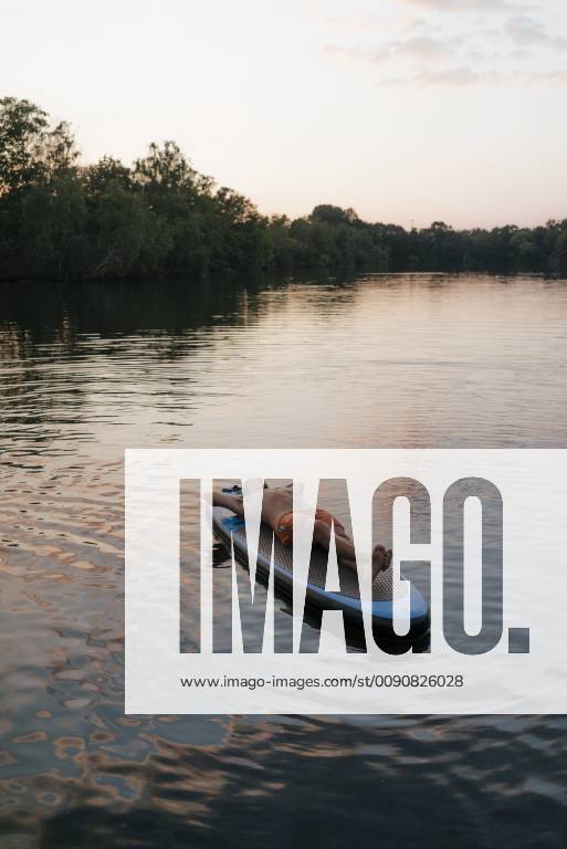 Man lying on SUP board on a lake at sunset model released Symbolfoto GUSF01831