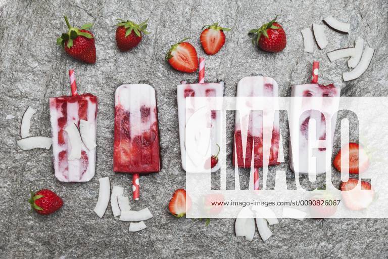 Homemade strawberry coconut ice lollies with fresh strawberries and coconut slices on granite GWF05710