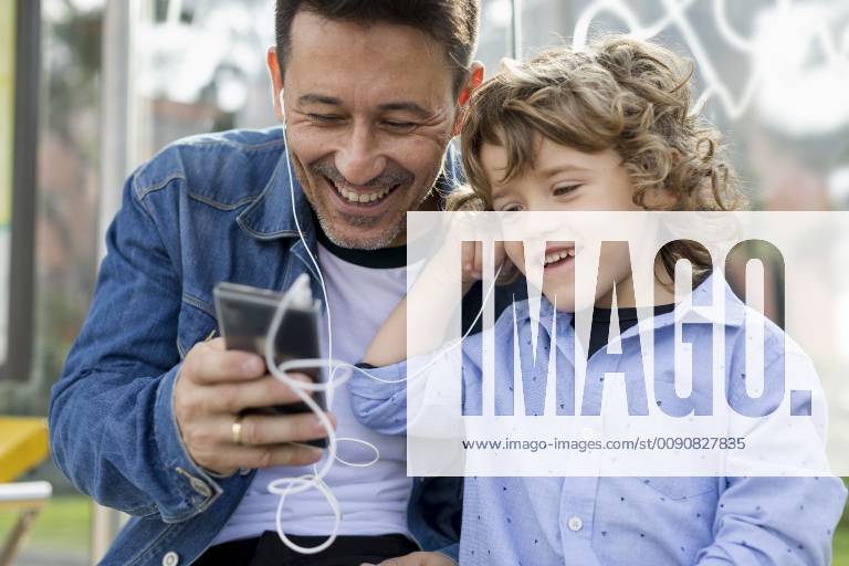 Happy father and son sharing cell phone and earbuds model released Symbolfoto MAUF02274