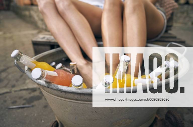 Friends relaxing in a backyard in summer, young women cooling their feet in a tub with drinks model released Symbolfoto property released PDF01859