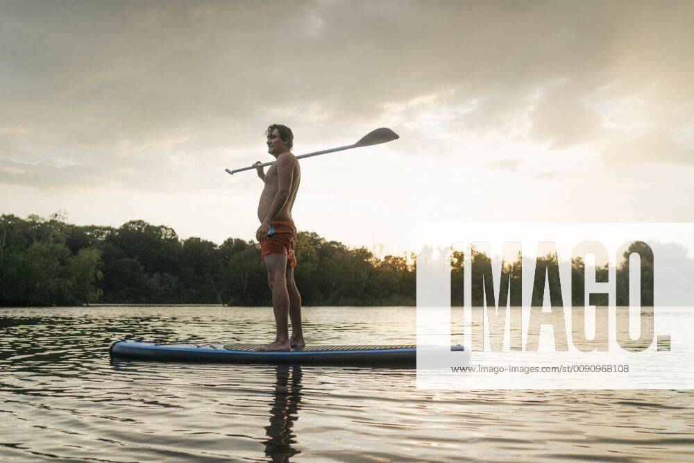 Man standing on SUP board on a lake at sunset model released Symbolfoto GUSF01826