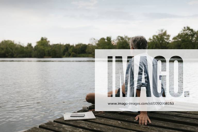 Senior man sitting on jetty at a lake model released Symbolfoto GUSF01839