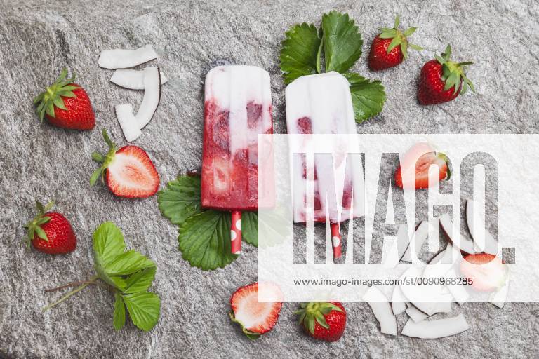 Homemade strawberry coconut ice lollies with fresh strawberries and coconut slices on granite GWF05711