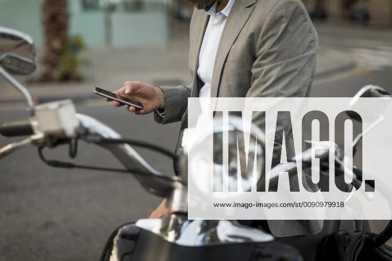 Close-up of businessman on motorscooter checking cell phone model released Symbolfoto MAUF02041
