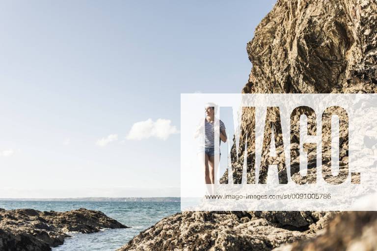 Young woman hiking on a rocky beach, looking at view model released Symbolfoto UUF16465