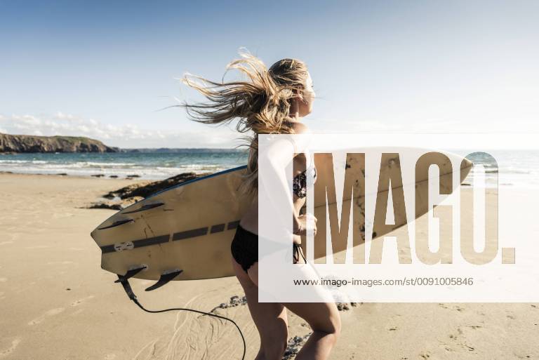 Young woman running on the beach, carrying surfboard model released Symbolfoto UUF16488
