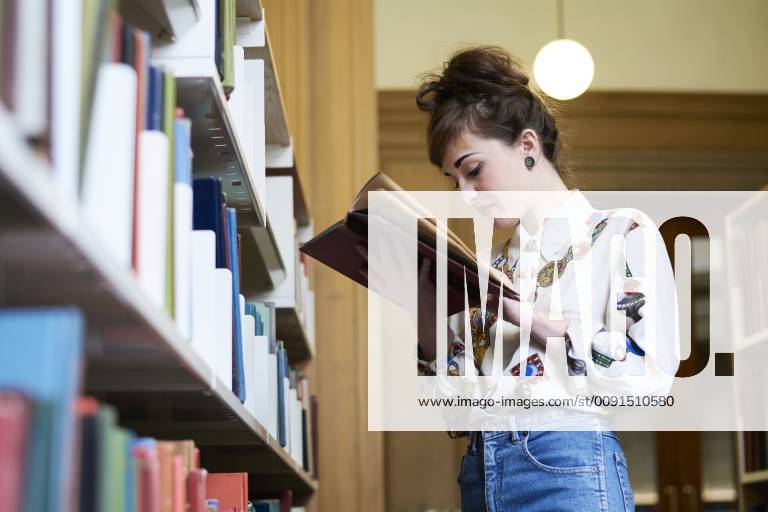 Female student reading book in a public library model released Symbolfoto IGGF01030