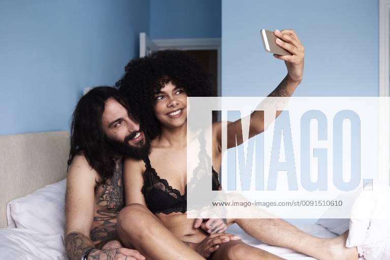 Happy affectionate young couple taking a selfie in bed model released Symbolfoto property released IGGF01068