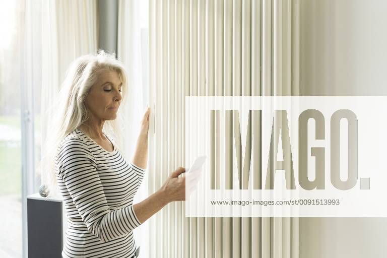 Mature woman with smartphone checking heating in living room of smart home model released Symbolfoto property released SBOF01886