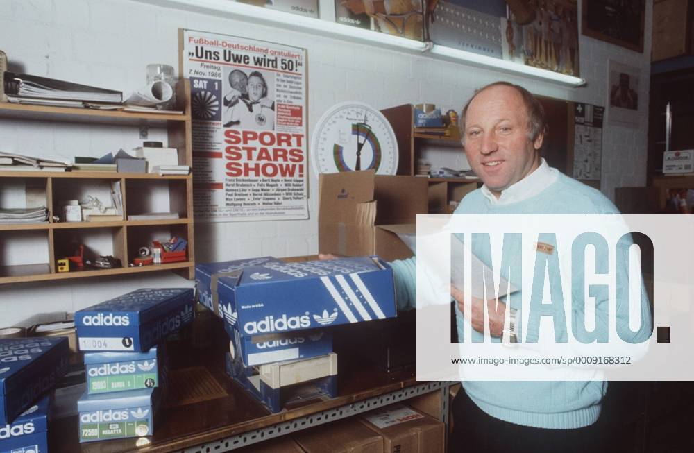 Uwe Seeler (Ex-Fußballnationalspieler) 10 86 ru Mann Fußball Nationalmannschaft grauhaarig Halbglatze leger Pullover Hemd stehend Keller Poster Fotografie Karton Schuh Unterlagen Papier haltend halb quer