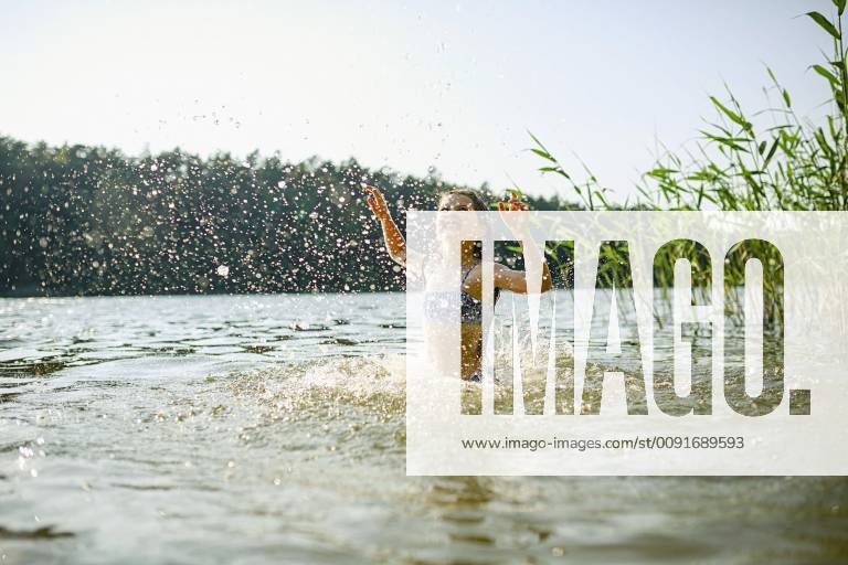 Playful girl splashing, swimming in sunny summer lake Germany Brandenburg