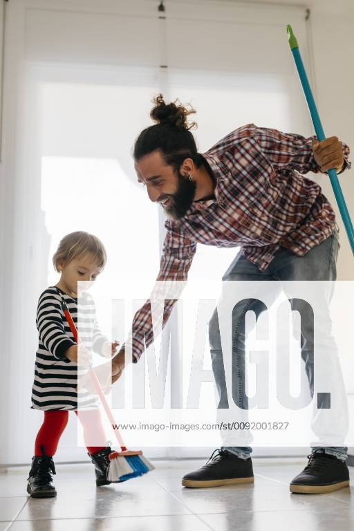 Happy father and little daughter sweeping the floor of the living room at home model released Symbolfoto property released JRFF02985