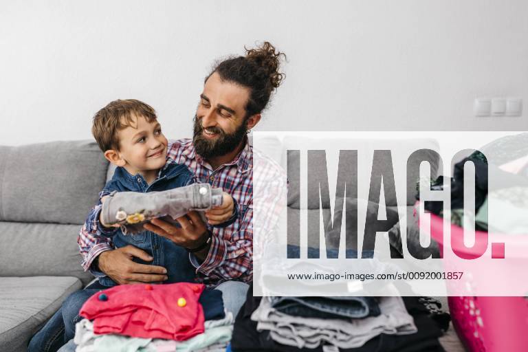 Portrait of happy father and son sitting together on the couch folding laundry model released Symbolfoto property released JRFF03011
