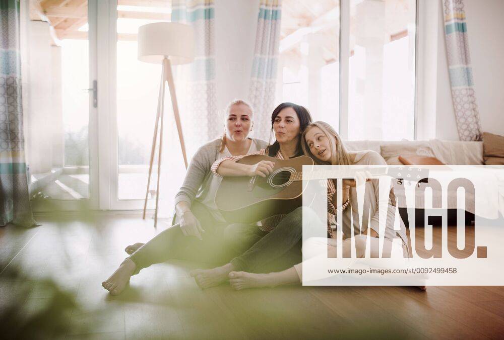 IMAGO Creative: Bildung, Musikerziehung Tag der Musik am 21. Juni Mature woman with two daughters sitting on the floor playing guitar at home model released Symbolfoto property released HAPF02965