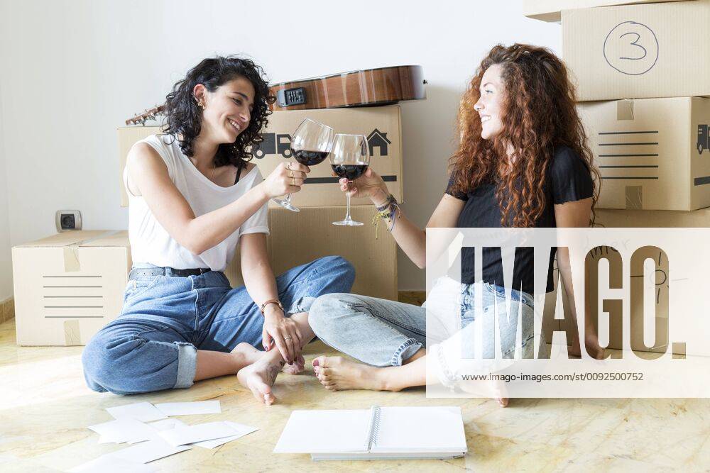Two friends moving into new home clinking red wine glasses model released Symbolfoto property released JPTF00224