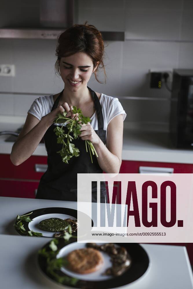 Smiling young woman garnishing plates of vegetarian food in her kitchen model released Symbolfoto property released LJF00087