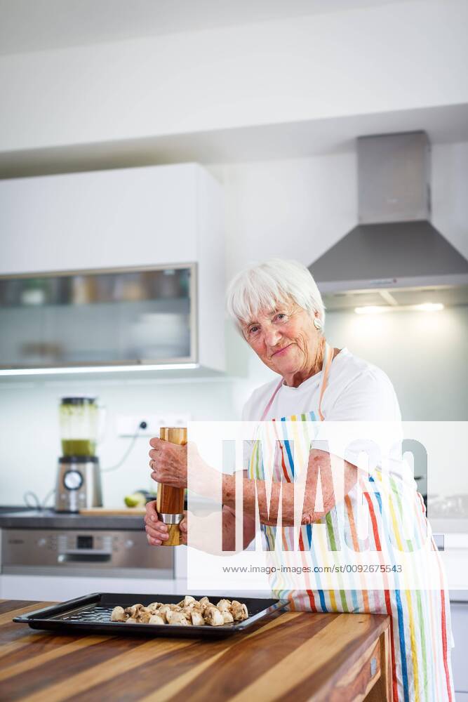 Senior woman cooking in the kitchen - eating and cooking healthy for her family putting some potates in the oven, enjoying active retirement (shallow DOF color toned image) ,model released, Symbolfoto