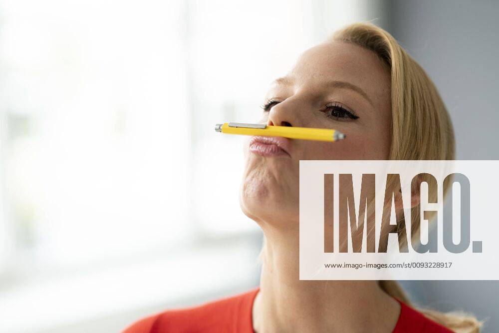Playful young woman balancing pen on her mouth in office model released Symbolfoto property released JOSF03469