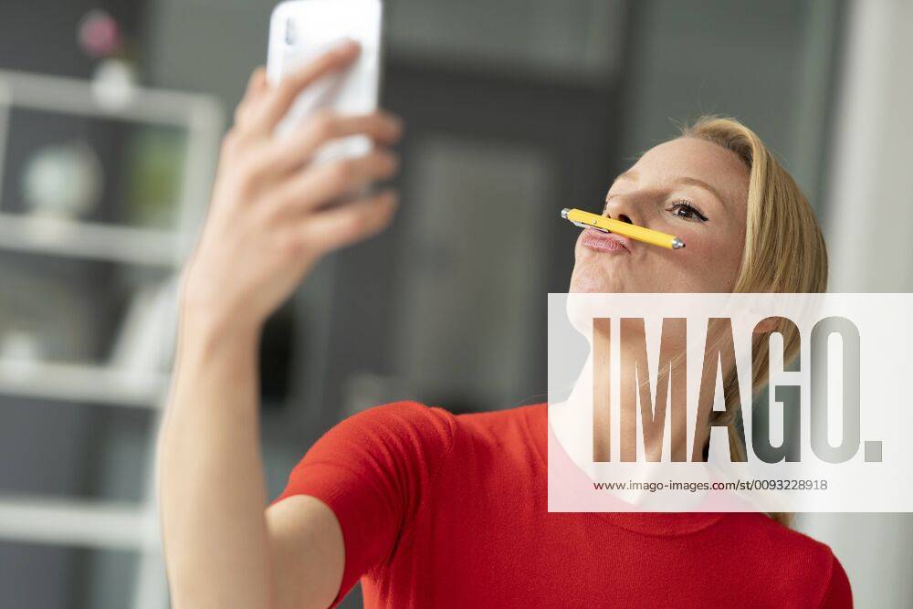 Playful young woman balancing pen on her mouth in office taking a selfie model released Symbolfoto property released JOSF03470