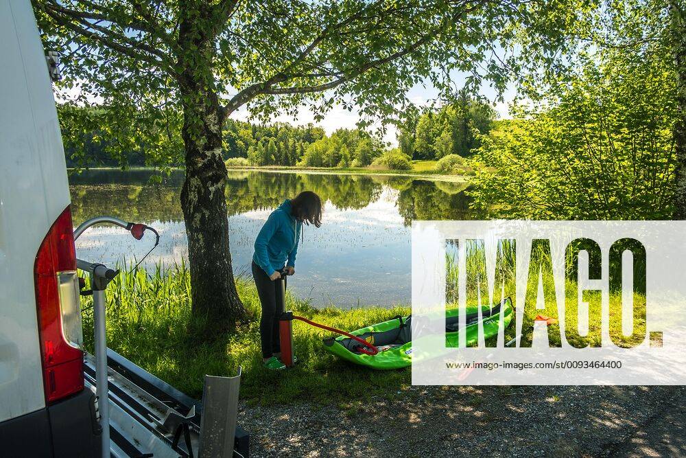 A girl pumps up her kayak next to a camping bus to paddle on the lake, Wuhrmühleweiher, Kisslegg in the Allgäu, Baden Württemberg, Germany Kayak tour at a pond in the Allgäu