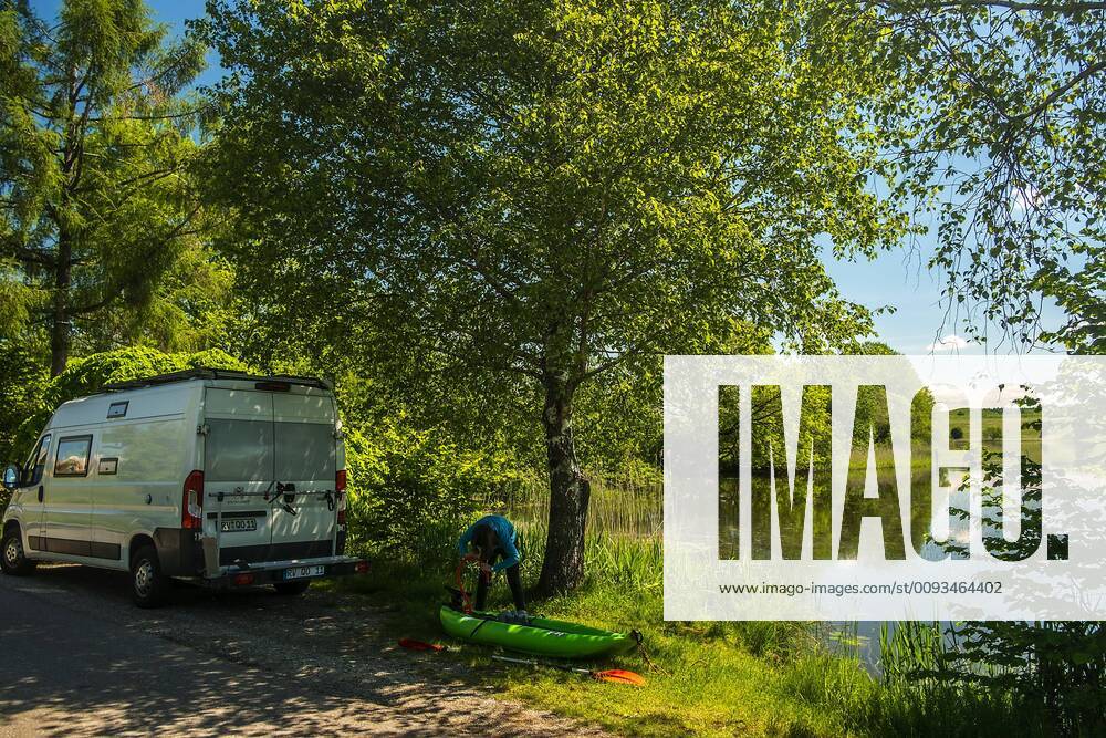 A girl pumps up her kayak next to a camping bus to paddle on the lake, Wuhrmühleweiher, Kisslegg in the Allgäu, Baden Württemberg, Germany Kayak tour at a pond in the Allgäu