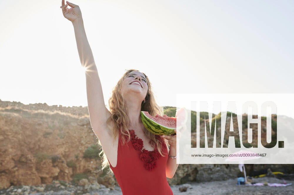 Carefree young woman holding watermelon slice on the beach model released Symbolfoto IGGF01315