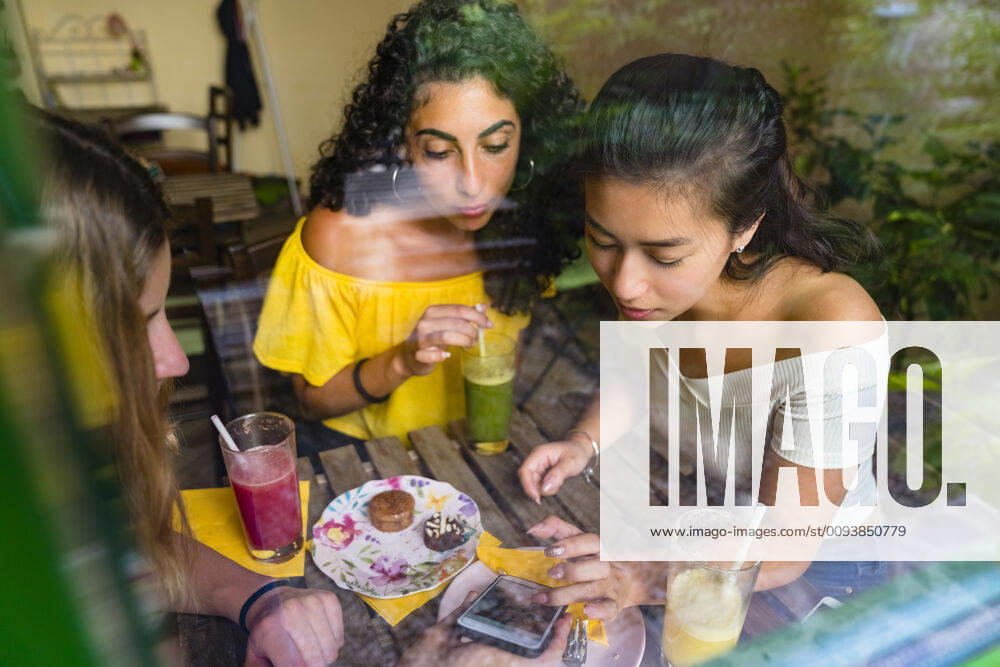 Three young women with smoothies meeting in a cafe sharing smartphone model released Symbolfoto property released MGIF00688