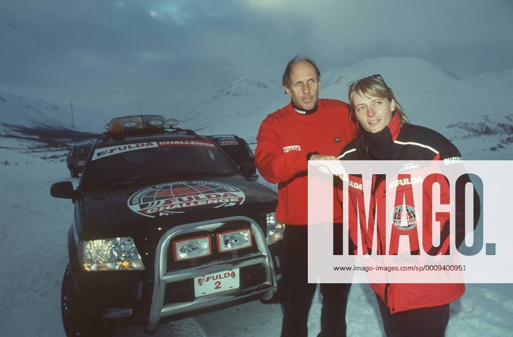 Jutta Kleinschmidt und Hans-Joachim Stuck im Yukon- Territorium (Kanada) 02 00 mapo Motorsportlerin Motorsport Auto Autosport Rallyes Rallye Rallyesport Rallyefahrerin Rallyefahrer Fahrerin Fahrer leger sportlich rot-schwarz stehend draussen vor Auto PKW Wagen Logo Fulda halb quer lächelnd Gespräch sich umschauend etwas beobachtend suchend