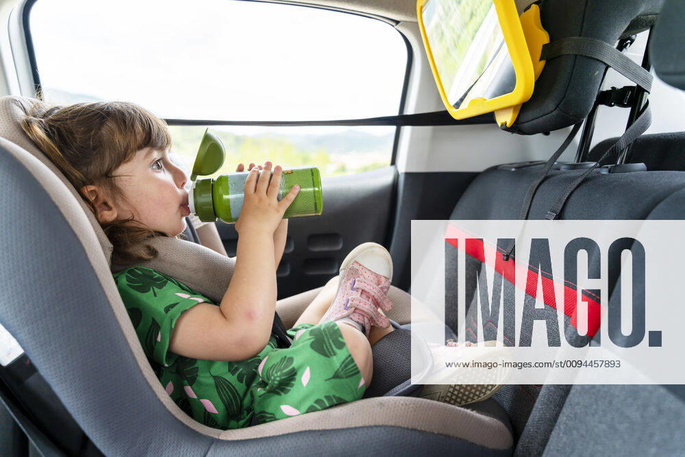 Toddler girl sitting on a car seat with a mirror drinking water model released Symbolfoto GEMF03149
