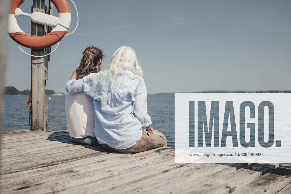 Mother and daughter looking at the sea, sitting on jetty, rear view model released Symbolfoto JOSF03710