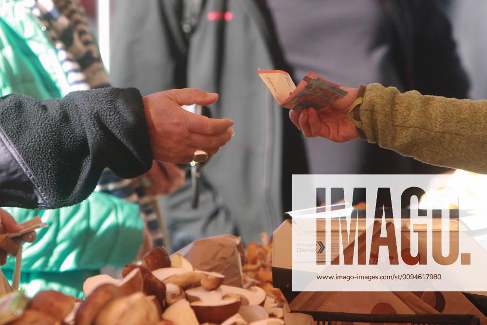 Woman hands a market seller a euro banknote to pay for her purchased goods Viktualienmarkt in Munich, Bavaria, Germany